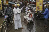 Street scene from Mumbai. To the left, a man on his bike and in the centre, several men looking directly into the camera.