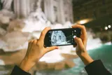 Photo: Two hands holding a mobile and photographing Fontana di Trevi in Rome.