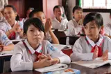 Vietnamesiske skoleelver i skoleuniform sidder ved deres skrivepult og klapper.